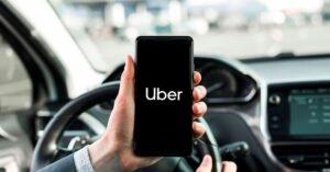A imagem mostra uma pessoa dentro de um carro segurando um celular com a logo do Uber na tela para representar o Uber para idosos