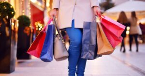A imagem mostra uma mulher segurando sacolas de compras para representar as vendas do Dia das Mães