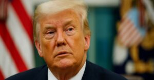 Donald Trump com expressão séria diante de bandeiras dos Estados Unidos, em imagem relacionada às tarifas dos EUA sobre aço e alumínio impostas durante seu governo.
