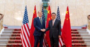 Autoridades dos EUA e da China apertando as mãos diante das bandeiras de seus países.
