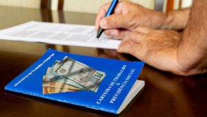 Carteira de trabalho com cédulas de reais sobre a mesa representa a taxa de juros do consignado privado para trabalhadores CLT.