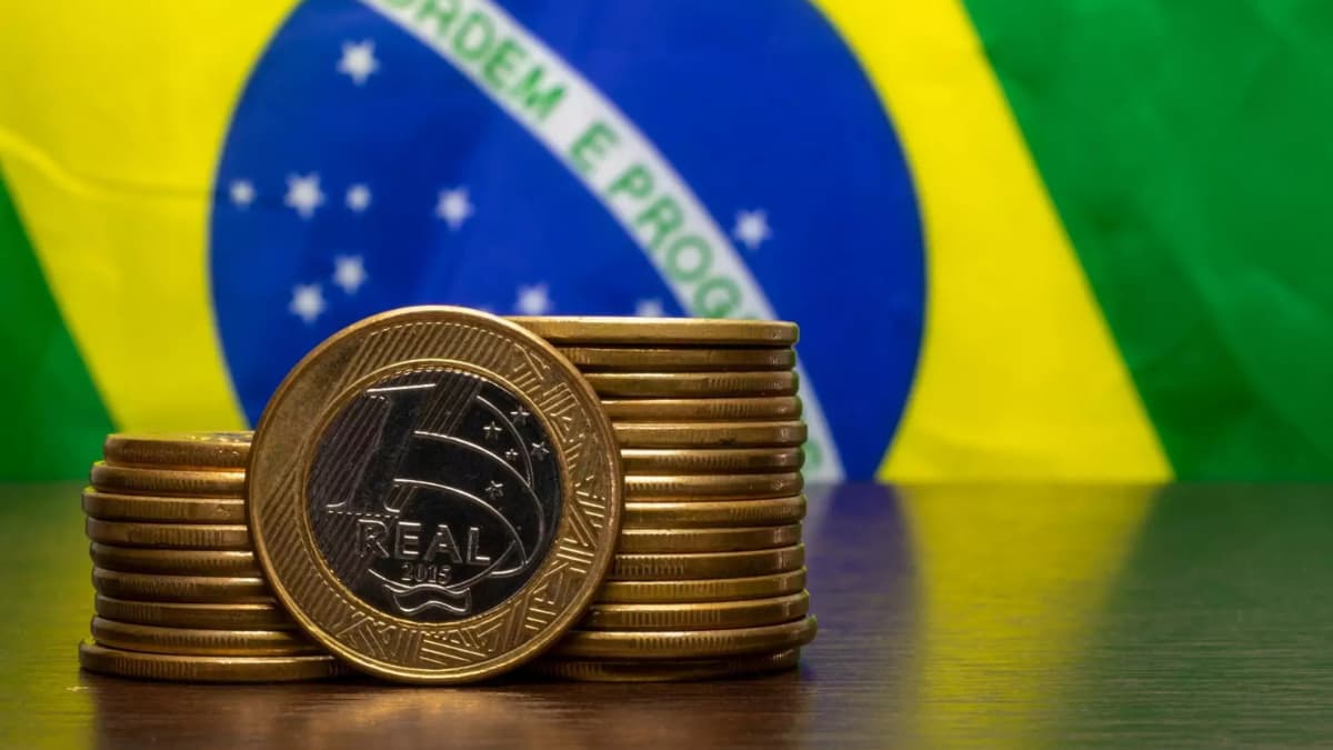Moedas de um real empilhadas à frente da bandeira do Brasil, simbolizando a trajetória da dívida pública brasileira