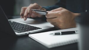 Pessoa com cartão de crédito digitando em notebook, ilustrando o processo em que a CAIXA digitaliza financiamento de imóveis