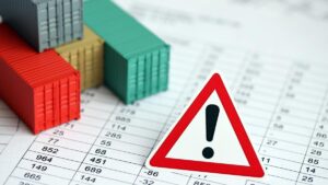 Containers sobre planilha de dados com placa de alerta, simbolizando urgência na regulamentação da Lei da Reciprocidade Econômica.