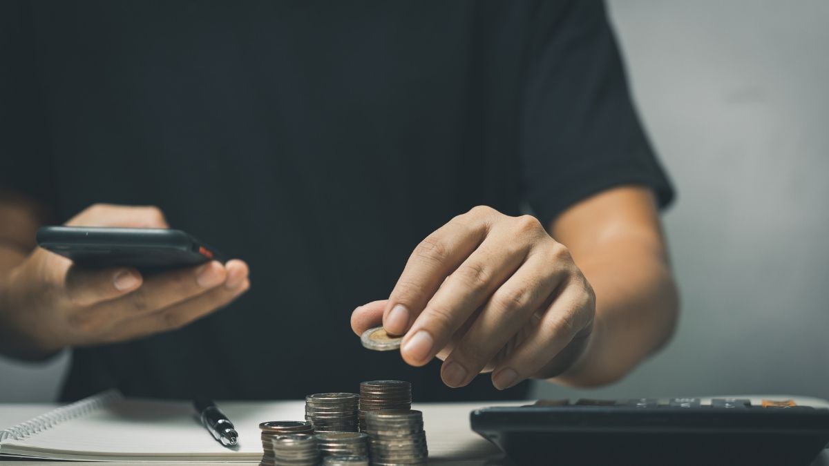 Homem calcula moedas e usa celular, representando projeção de inflação para 2025