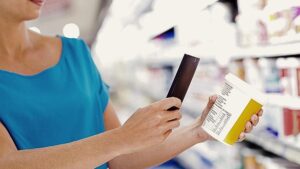 Mulher escaneia código de barras de embalagem com celular em supermercado, verificando a identificação correta de produtos GTIN/EAN.