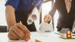Incentivo a construtoras em São Paulo — profissionais analisam projetos habitacionais com maquete e capacete de obra sobre a mesa.