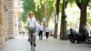 Mulher andando de bicicleta em rua europeia arborizada, ilustrando o custo de vida na Irlanda em 2025