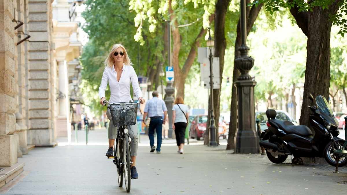 Mulher andando de bicicleta em rua europeia arborizada, ilustrando o custo de vida na Irlanda em 2025