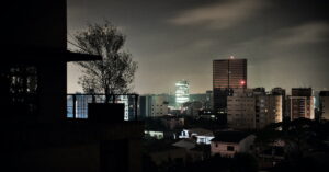 Vista noturna de cidade brasileira durante apagão nacional, com parte dos prédios sem luz e horizonte parcialmente iluminado.