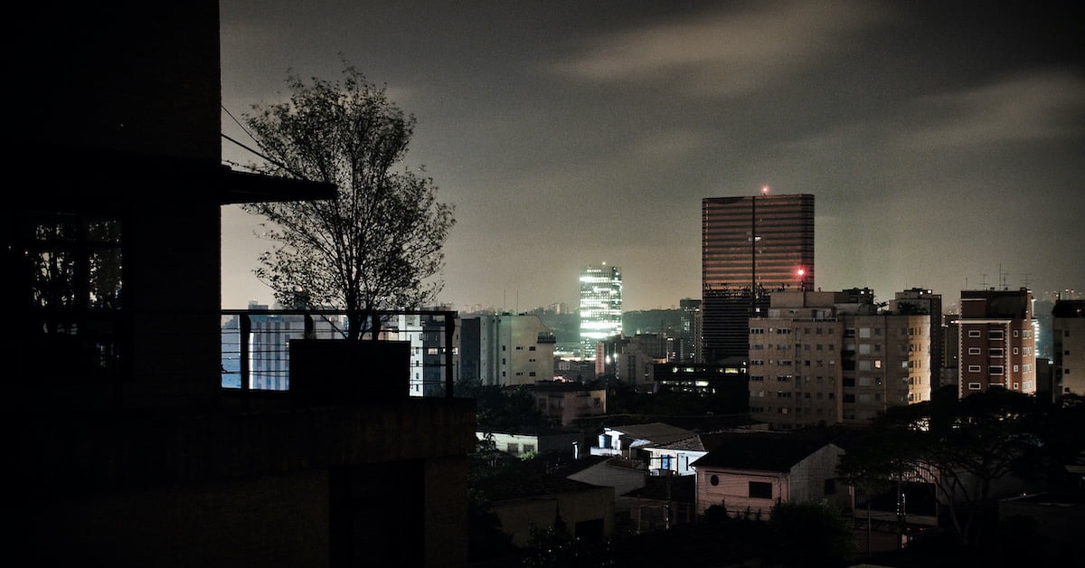 Vista noturna de cidade brasileira durante apagão nacional, com parte dos prédios sem luz e horizonte parcialmente iluminado.
