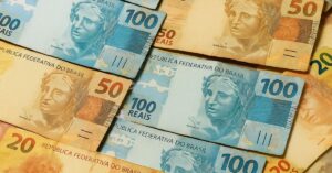 Notas de 100, 50 e 20 reais dispostas sobre uma mesa, representando o pagamento de salários no quinto dia útil de outubro.