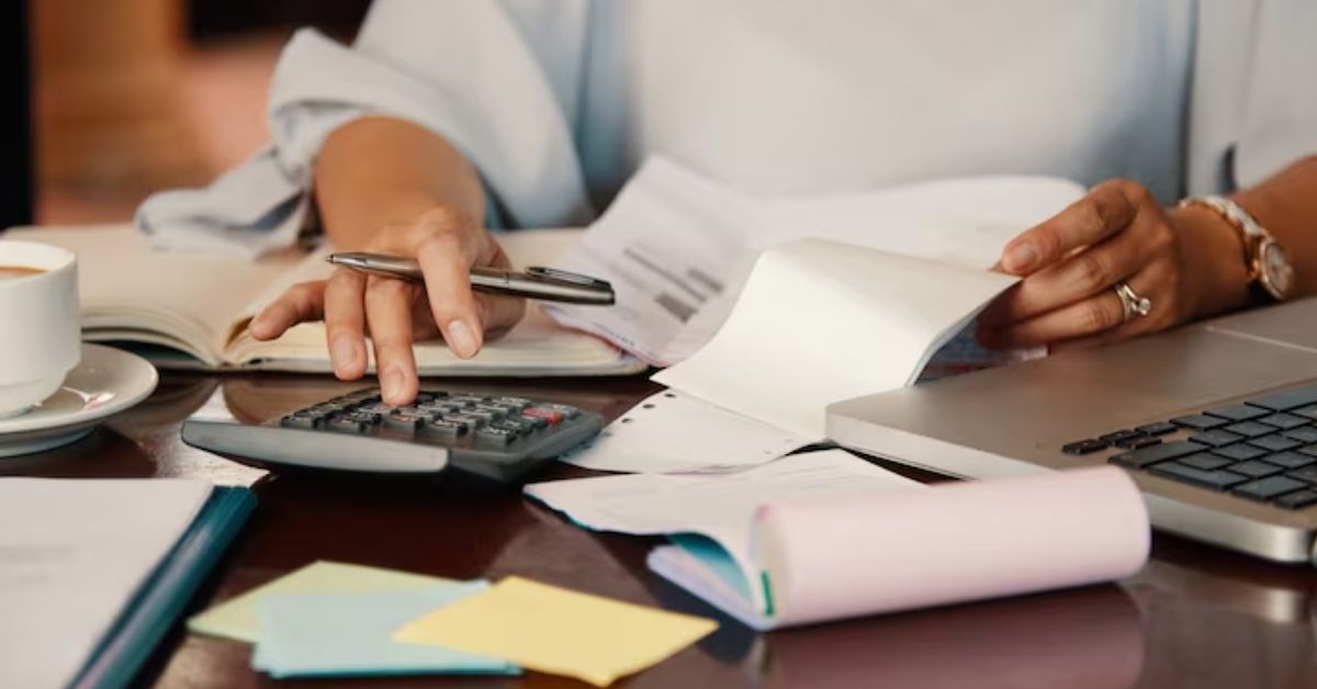 Mulher calculando contas em meio a papéis, representando a inadimplência no sistema financeiro.