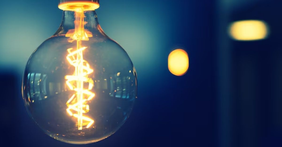 Lâmpada incandescente acesa com fio visível e fundo difuso em azul.