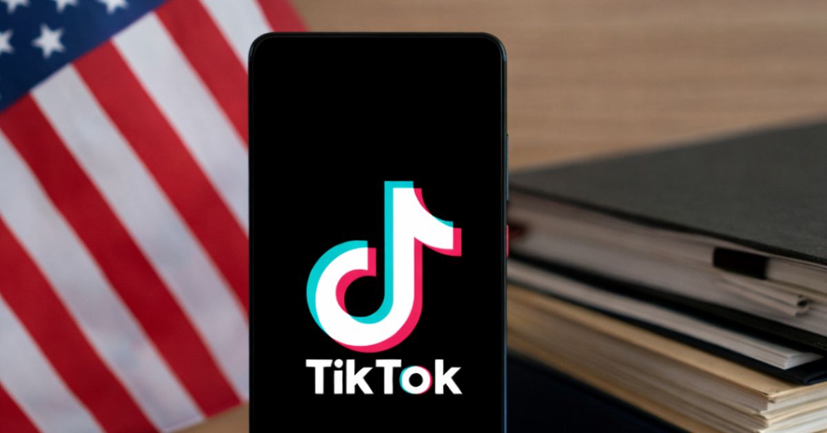 Smartphone com logotipo do TikTok sobre mesa ao lado de documentos e bandeira dos Estados Unidos.