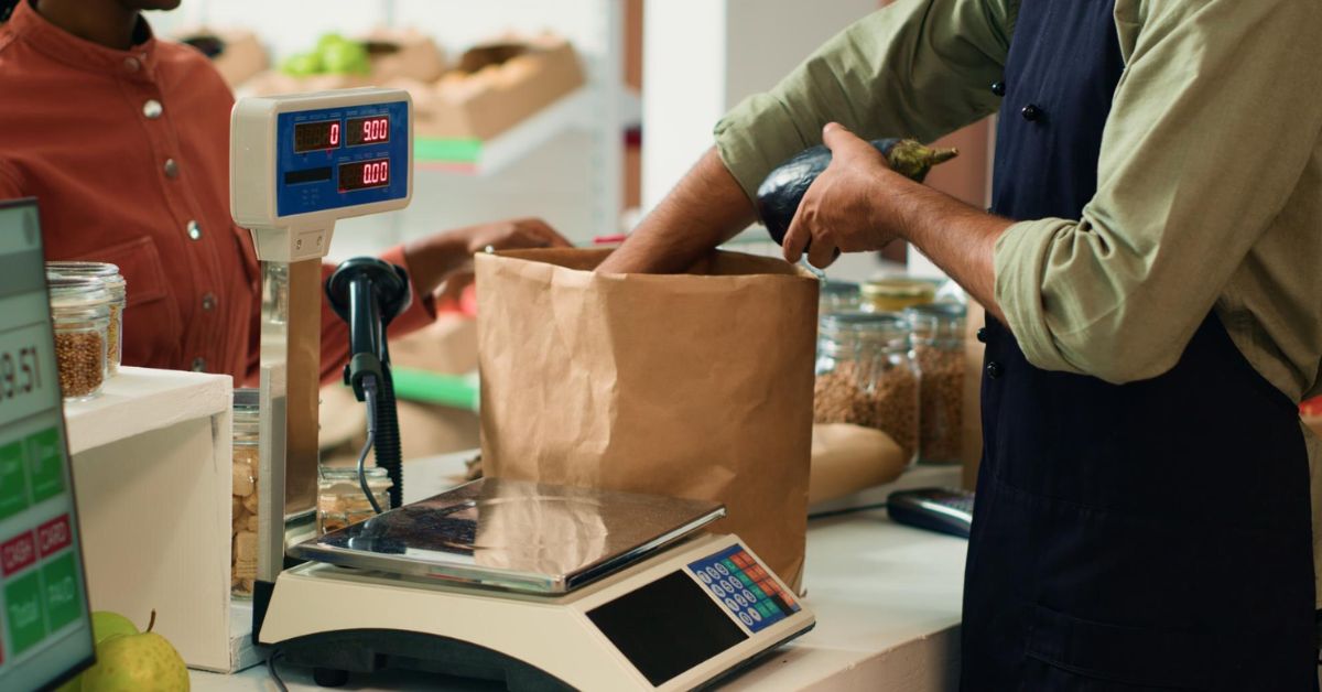 Compra em mercado com pesagem de alimentos no caixa durante cenário de pressão no consumo, representando confiança do comércio em abril