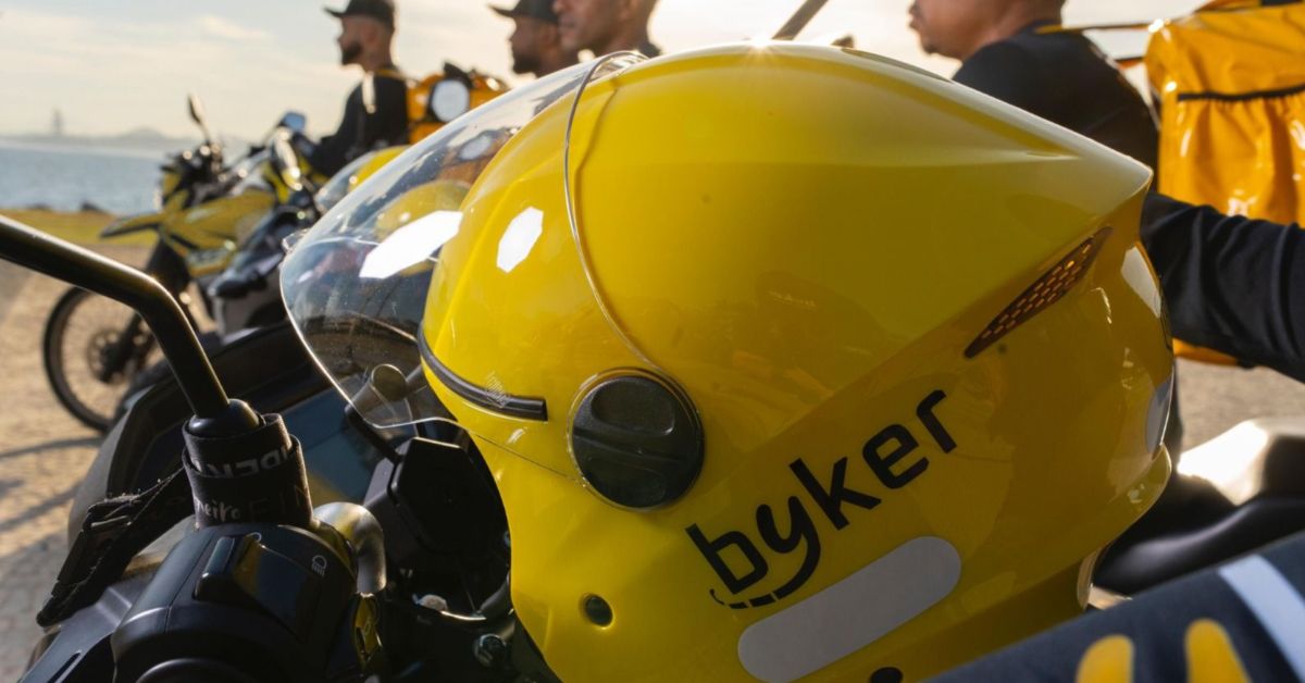 Entregadores com mochilas de delivery ao lado de motocicletas usadas em serviço de locação