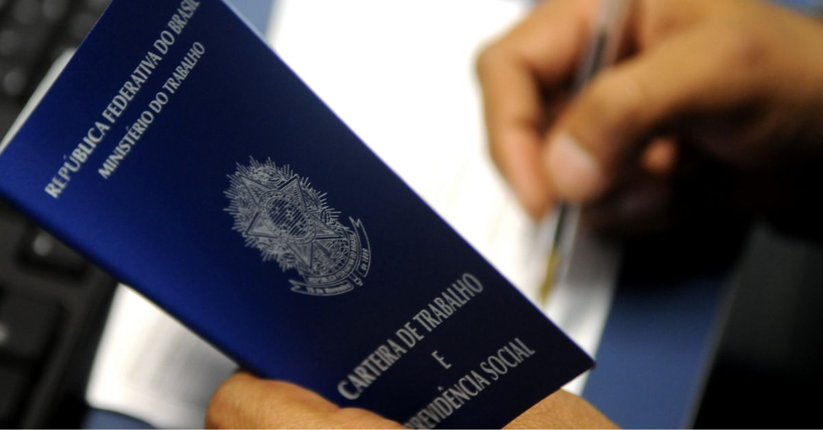 Carteira de Trabalho (CLT) sendo segurada enquanto trabalhador assina documento