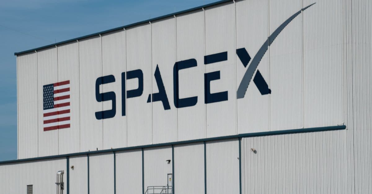 Fachada de galpão industrial da SpaceX com logotipo da empresa e bandeira dos Estados Unidos