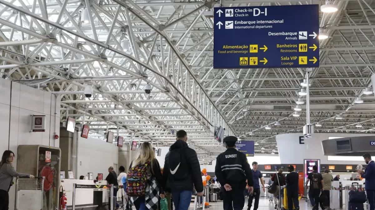 Passageiros circulam em aeroporto brasileiro com sinalização de embarque e serviços no terminal