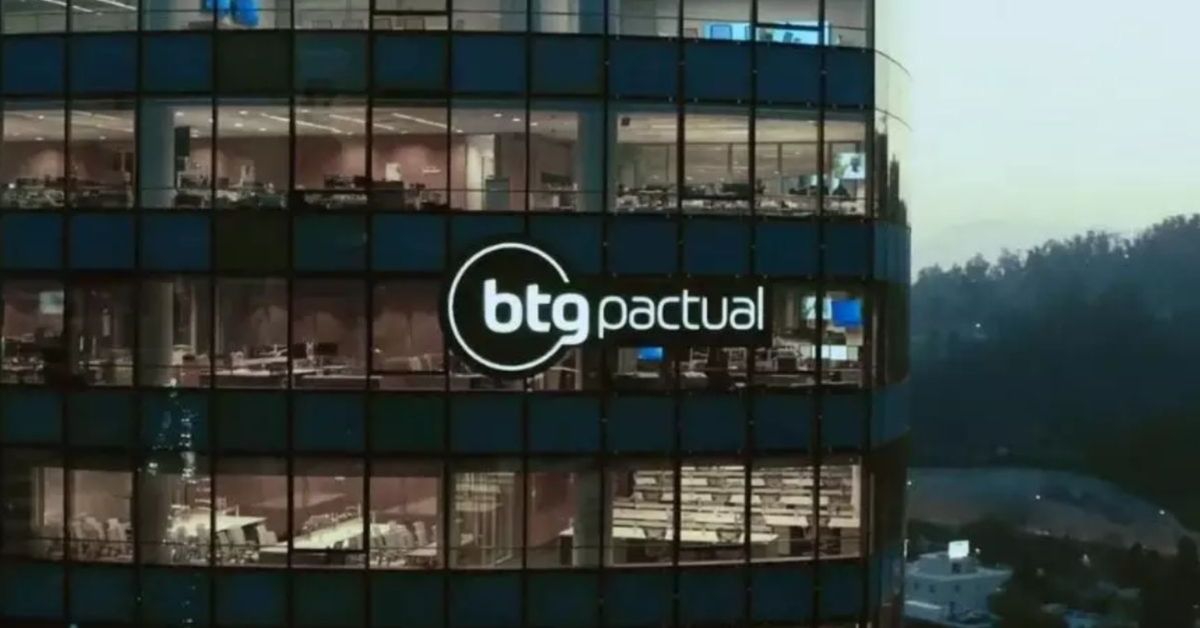 Prédio do BTG Pactual com logotipo iluminado na fachada de vidro durante o entardecer