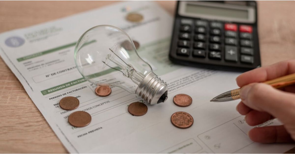 Conta de energia elétrica ao lado de calculadora, moedas e lâmpada, ilustrando o aumento dos custos de eletricidade e o impacto das tarifas no orçamento.