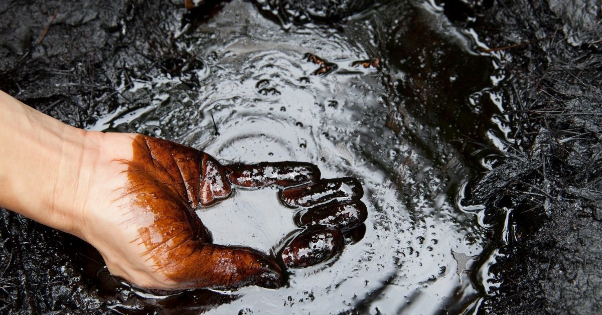 Mão coberta por petróleo cru em área escura com acúmulo de óleo no solo, representando descoberta de petróleo no Ceará