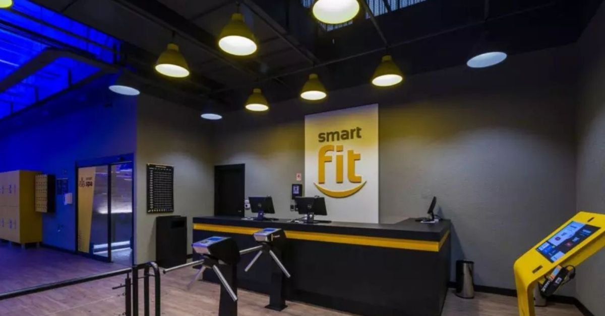 Recepção de academia da Smart Fit com logo da rede ao fundo e catracas de acesso na entrada simbolizando resultados do 1t26