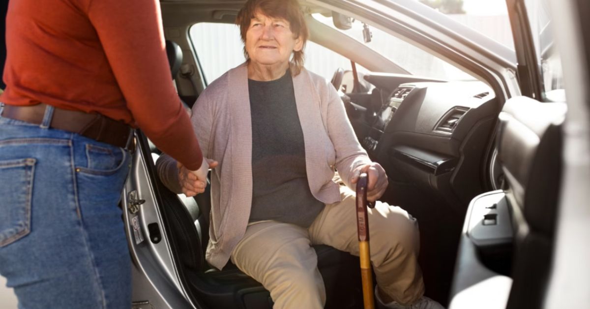 Idosa entra em carro com auxílio de acompanhante em serviço de mobilidade assistida voltado ao público 60+.