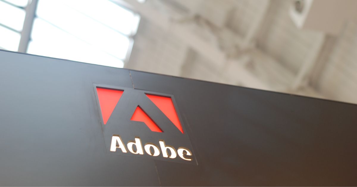 Logo da Adobe em painel corporativo, imagem usada em matéria sobre ações da Adobe, inteligência artificial e concorrência no mercado de software criativo.