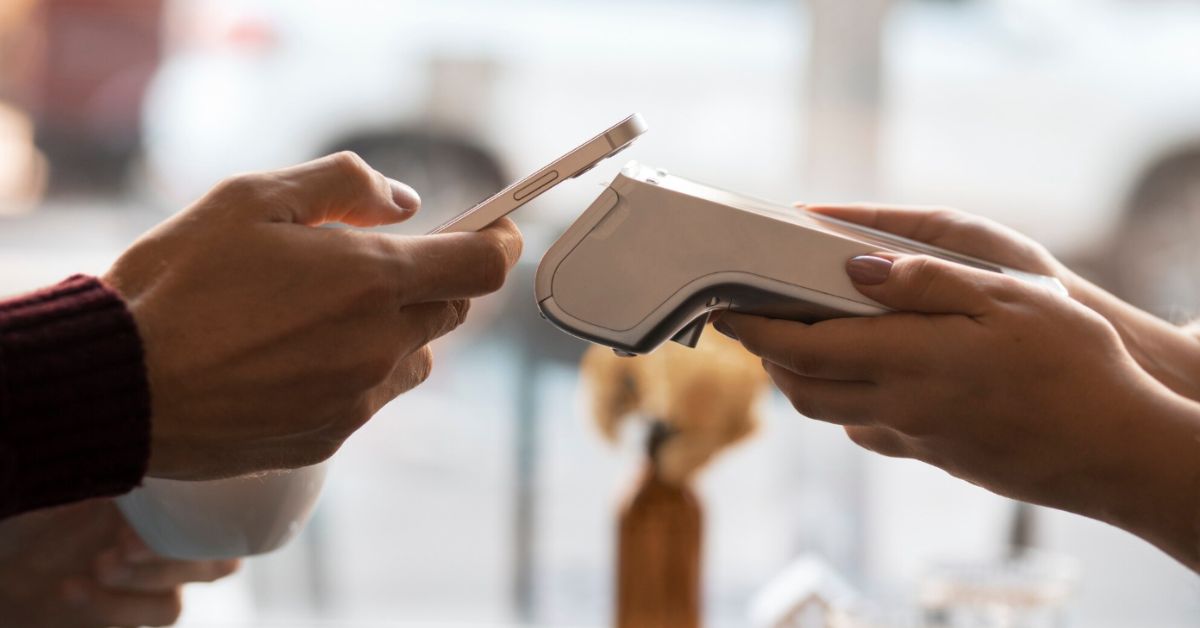Pessoa realiza pagamento por aproximação utilizando smartphone em uma máquina de cartão, ilustrando o uso de Pix por aproximação e carteiras digitais.