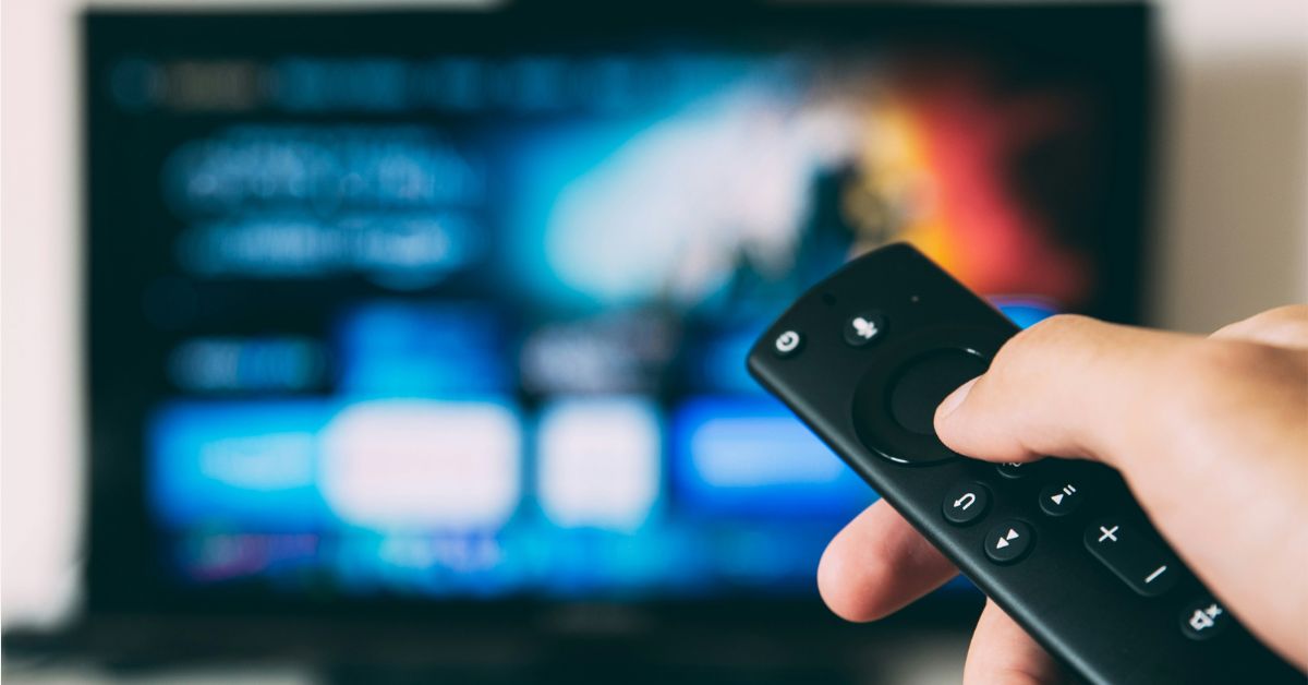 Controle remoto apontado para uma smart TV com interface de streaming desfocada ao fundo, ilustrando o crescimento das plataformas de vídeo sob demanda nos lares brasileiros.