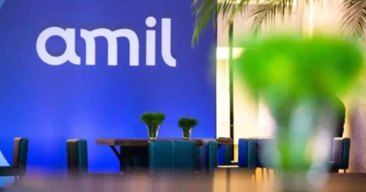 Recepção da Amil com logotipo da operadora em destaque em um painel azul, mesas e cadeiras ao fundo e um objeto desfocado em primeiro plano.